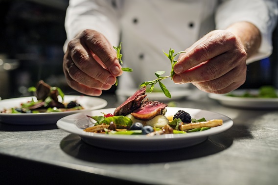 Chef adding the final flourish by adding some liquorice flavoured parsley to the dish. The dish is, pan fried pink duck breast onto a bed of parsnip puree with seasonal autumn vegetables and berries. Colour, horizontal with some copy space, photographed on location in a restaurant on the island of Møn in Denmark.