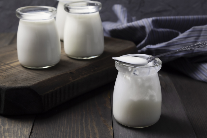 Natural homemade yogurt in glass jars with spoon on dark wooden background